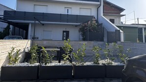A two-story house with a balcony, a covered carport, and a small garden area with plants and a table.