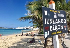 En välkomstskylt vid Junkanoo Beach, med fri sikt över stranden och ett kryssningsfartyg i bakgrunden.
