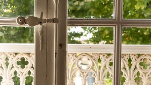 A close-up of a window with a white ornate grille, a metal latch, and a view of greenery outside. - Pélissanne in Provence (Pélissanne)