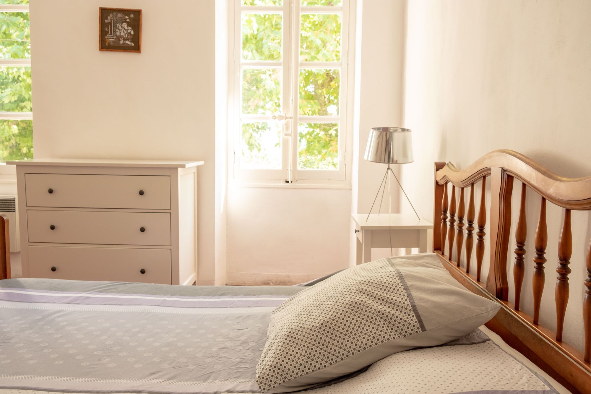 Une chambre à coucher comprenant un lit, une table de chevet, une commode et une fenêtre donnant sur des arbres.
