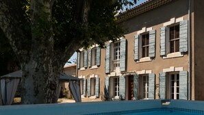 A swimming pool with a tiled edge, a building with blue shutters, and a large tree in the foreground. - Pélissanne in Provence (Pélissanne)
