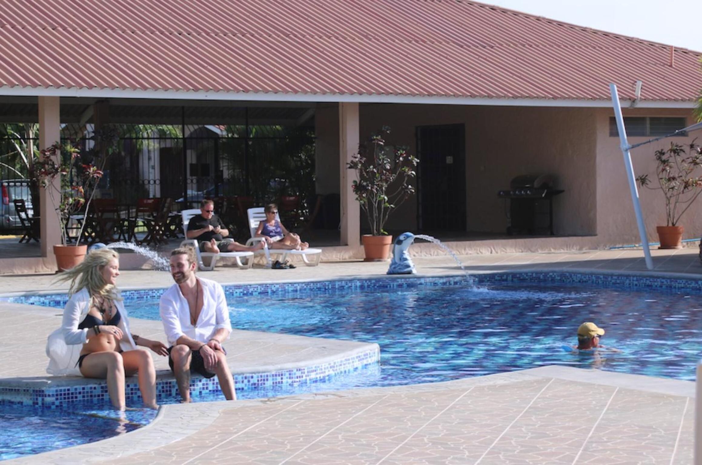 Zona de piscina con sillones de descanso y un área de estar cubierta.