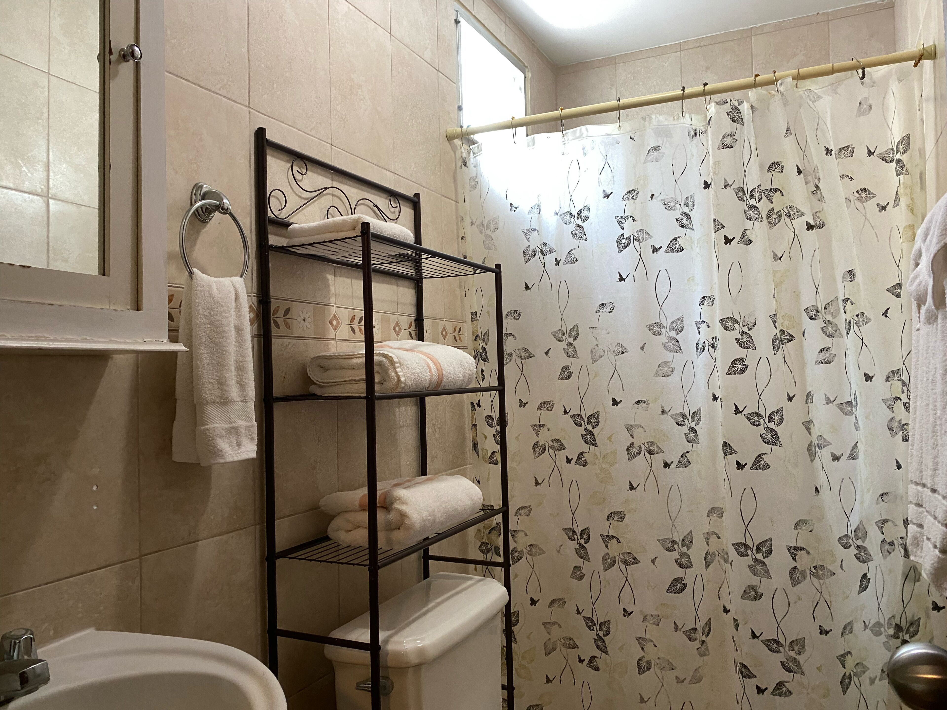 A bathroom with a toilet, a sink, a towel rack with towels, and a shower curtain with a leaf pattern.