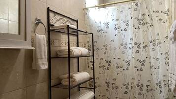 A bathroom with a toilet, a sink, a towel rack with towels, and a shower curtain with a leaf pattern.