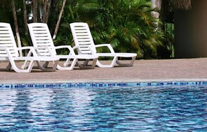 Una piscina al aire libre, sombrillas, sillones reclinables de piscina