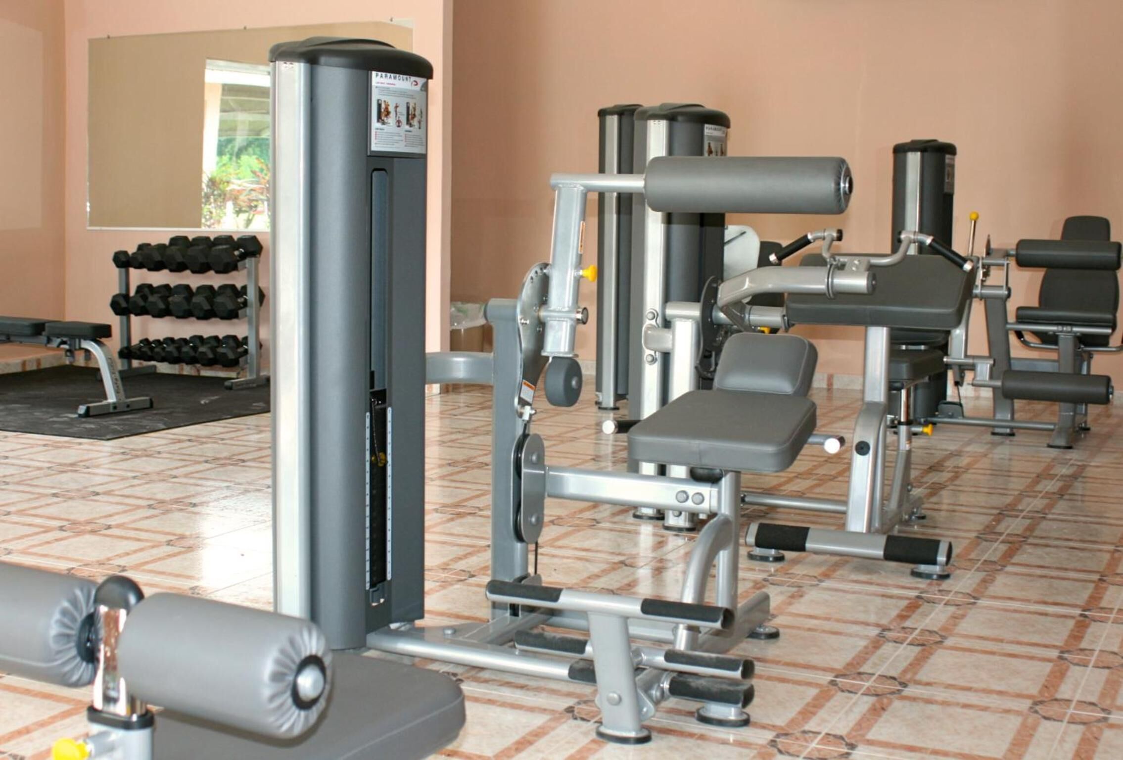 Une salle de sport équipée de divers appareils d’exercice, d’une rangée de haltères et d’un miroir au mur.