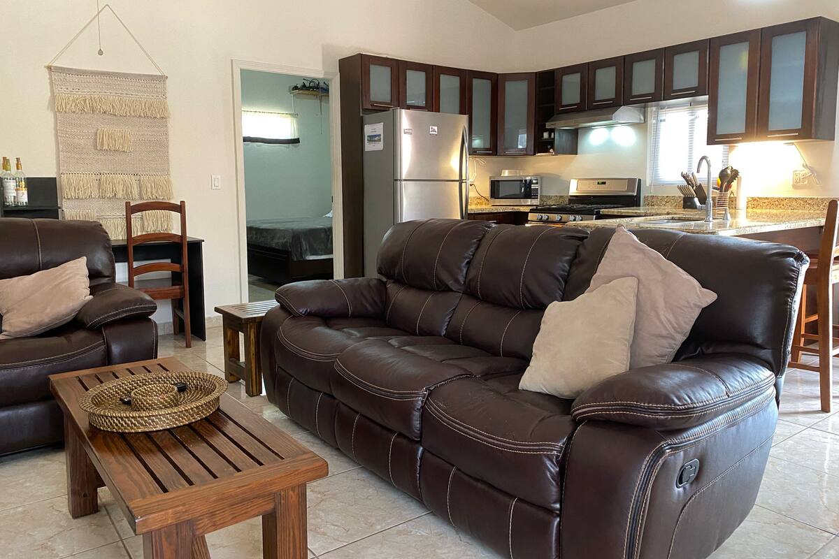 A living room with a brown leather sofa, a wooden coffee table, and a wall-mounted macrame piece.