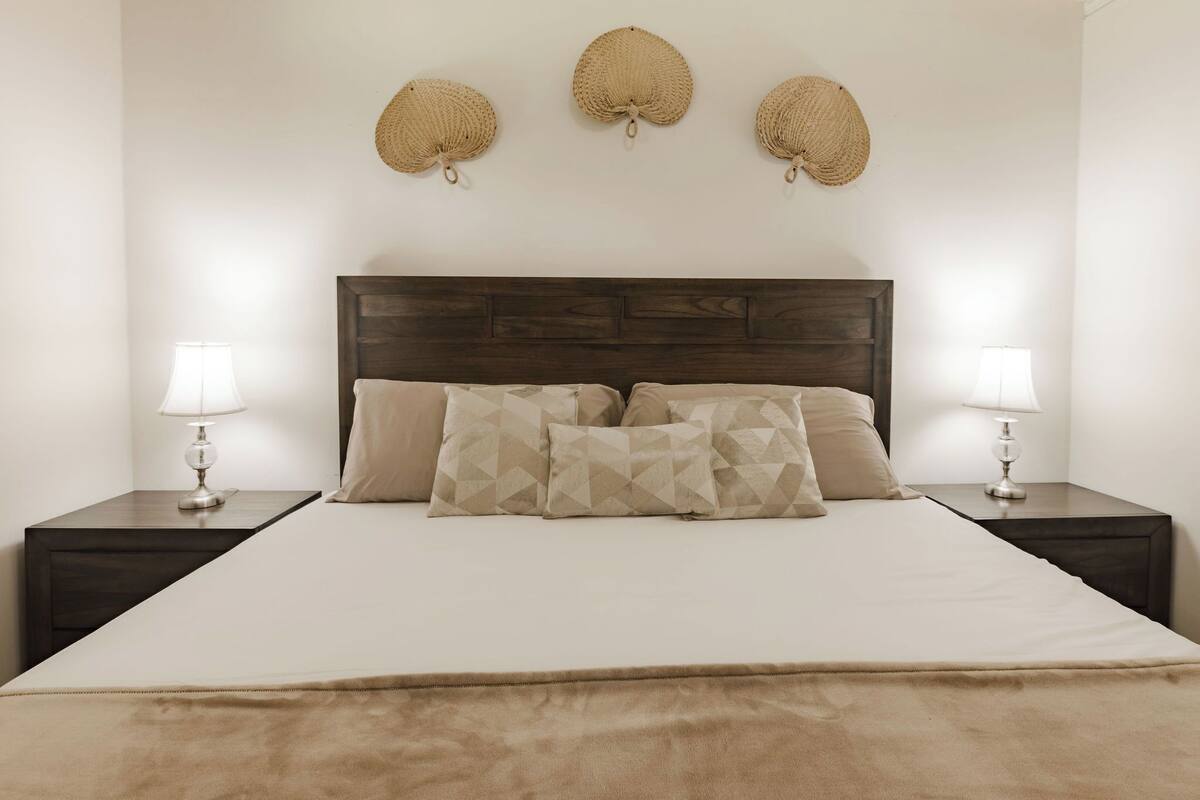 A neatly made bed with a wooden headboard, two bedside lamps, and three woven wall decorations.