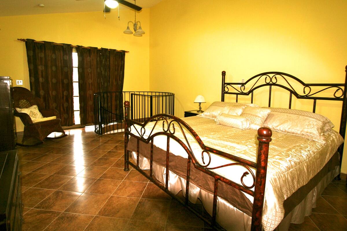 A bedroom with a wooden bed, a chair, a nightstand, and a window with curtains.
