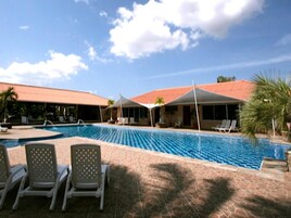 Una piscina con sillones de descanso y sombrillas, rodeada de edificios con tejados rojos.