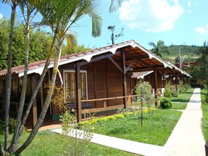 A wooden cabin with a tiled roof, surrounded by lush greenery and a clear sky. - Vale do Sonho Hotel & Eventos (Guararema)