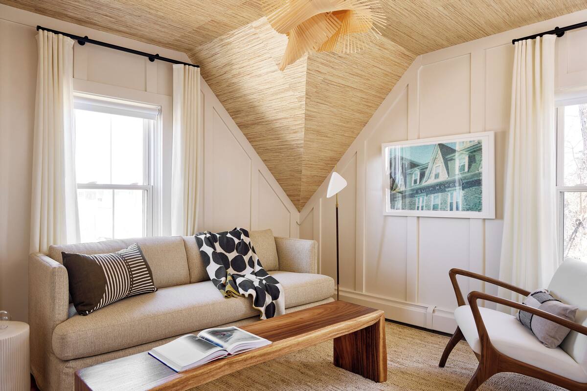 Una sala de estar acogedora con techo de madera, un sofá con cojines estampados, una mesa de centro y una silla.