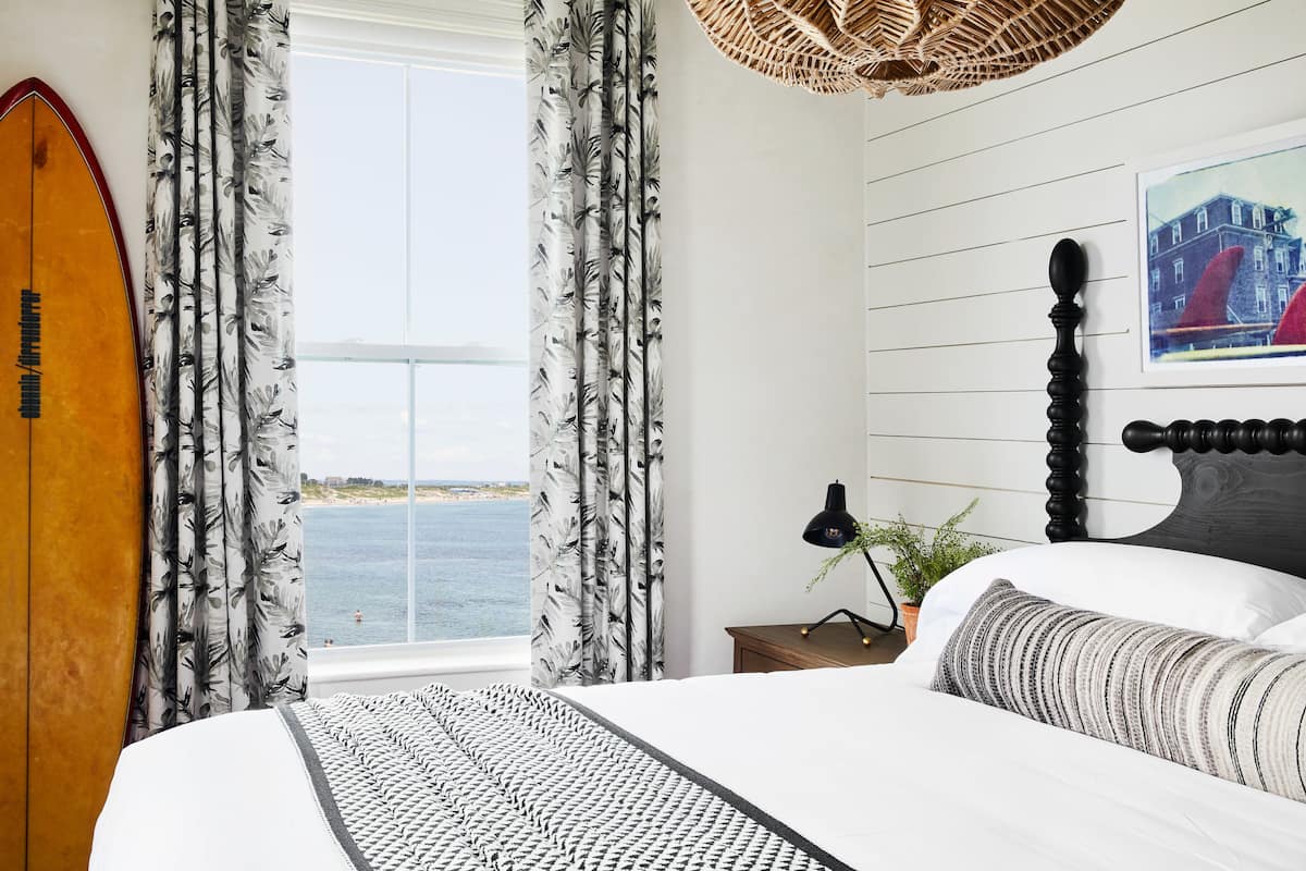 Un dormitorio con cama, cortinas, una tabla de surf, una lámpara y una planta.