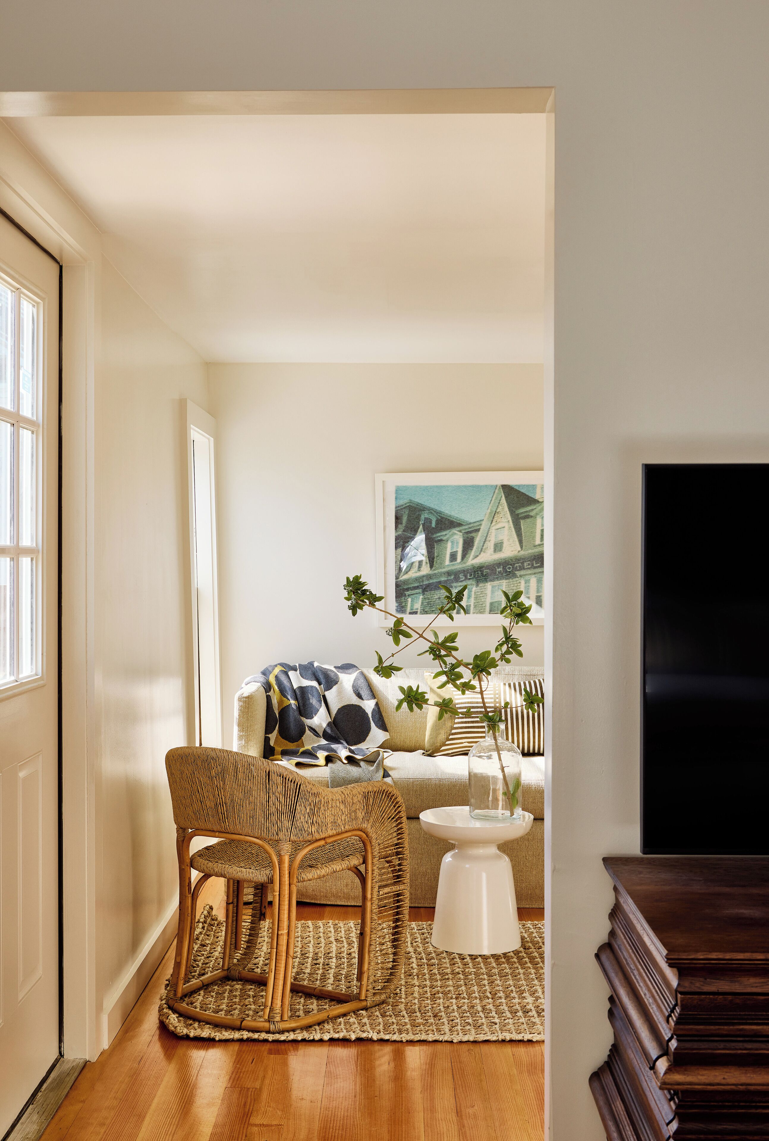 A living room with a wicker chair, a sofa, a small white table, and a framed picture on the wall.