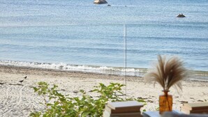 En utsikt över stranden med en träveranda, en vas med torkade växter och en avlägsen, klippig utskjutande del av landskapet.