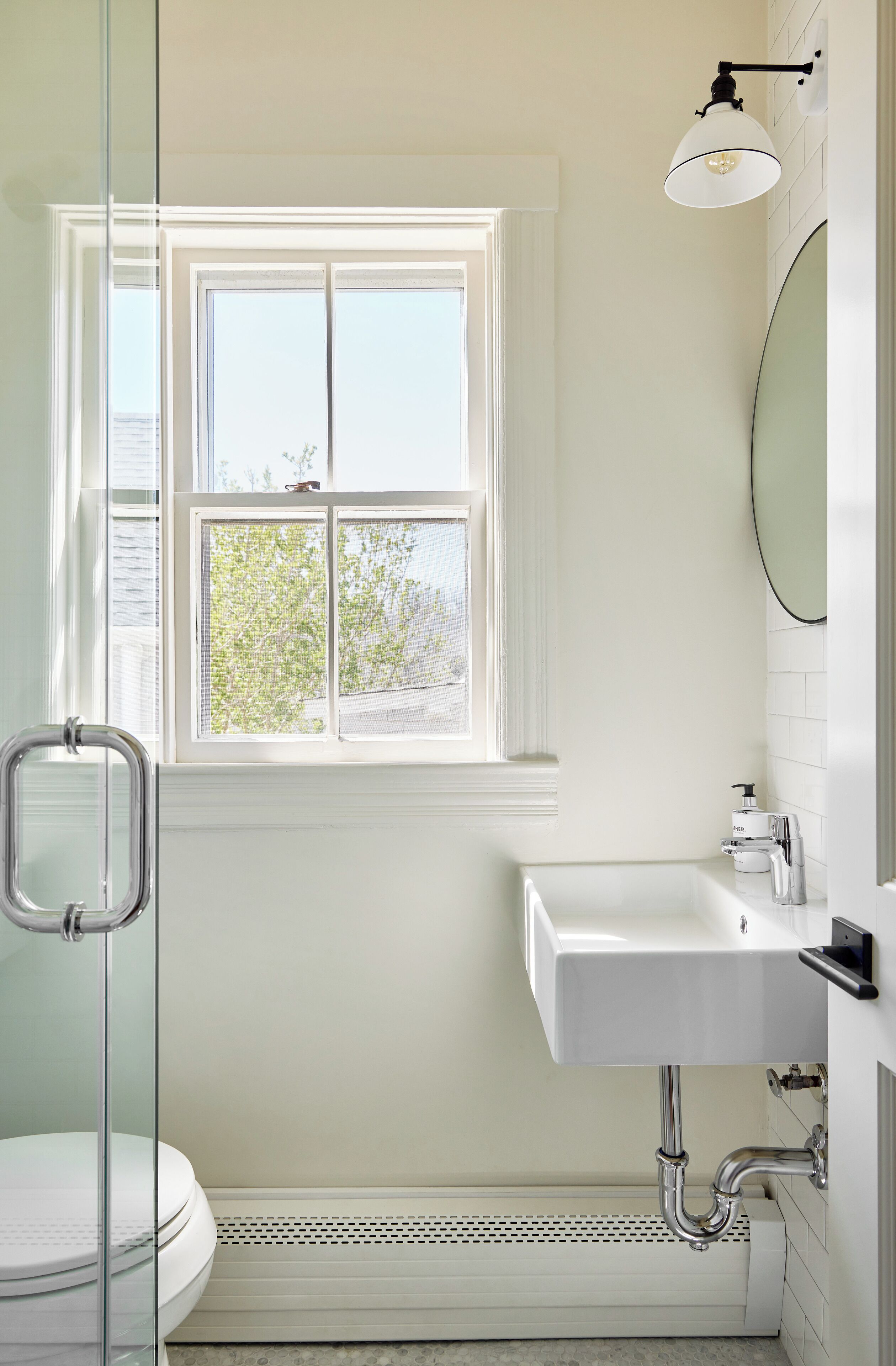 A bathroom with a window, a toilet, a sink, and a shower.