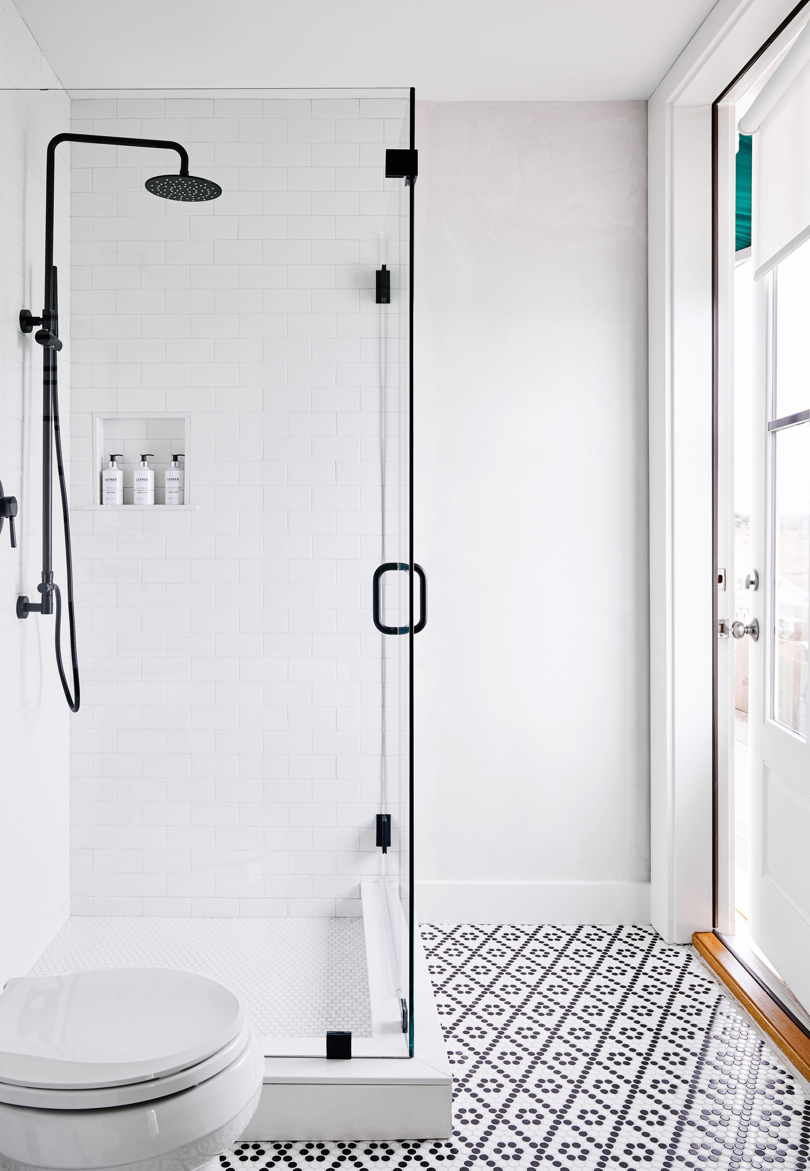 A modern bathroom with a white tiled shower, a toilet, and a patterned floor.