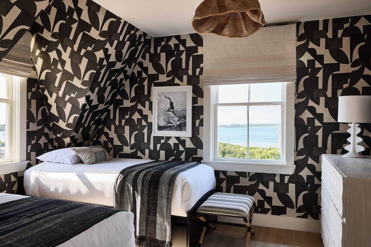 Un dormitorio con una cama, un banco y una ventana con vistas al mar.