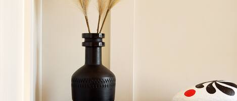 A dark wooden nightstand with a black vase containing pampas grass, a book titled "A Brief History of Surfing," and a pillow with a black and white design.