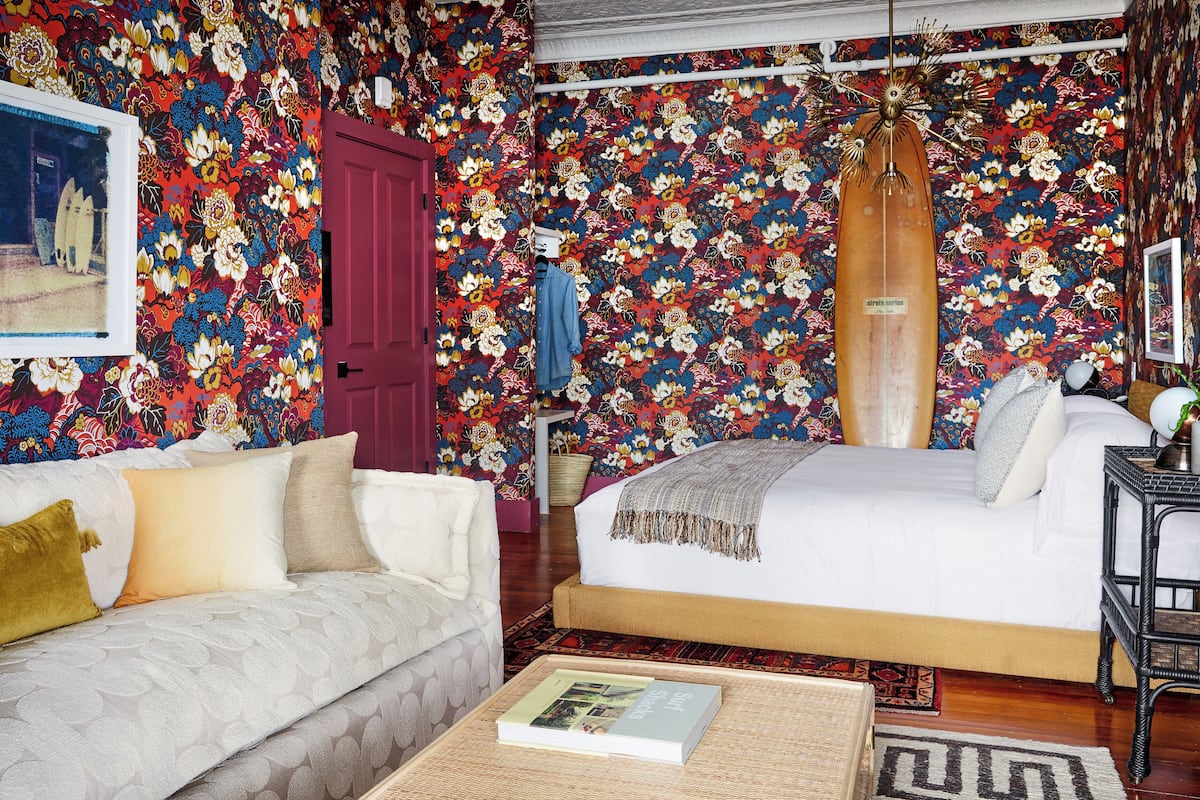 Un dormitorio con papel tapiz floral, una cama, un sofá y una lámpara colgante.