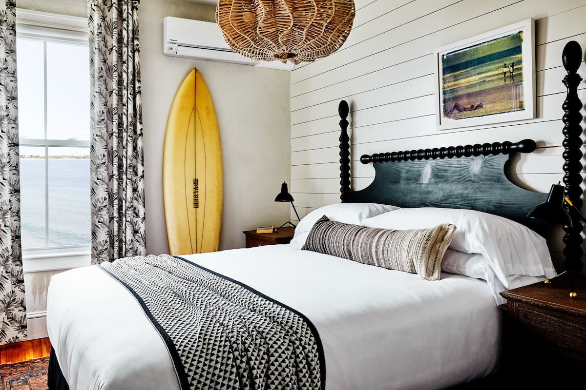 Un dormitorio con cama, una tabla de surf, una lámpara y vista al mar.