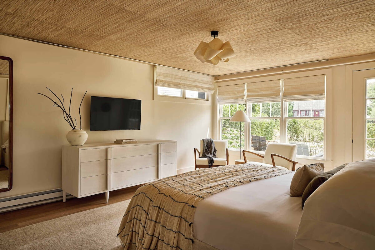 Un dormitorio con una cama grande, un aparador, un televisor y una ventana con vistas a la vegetación.