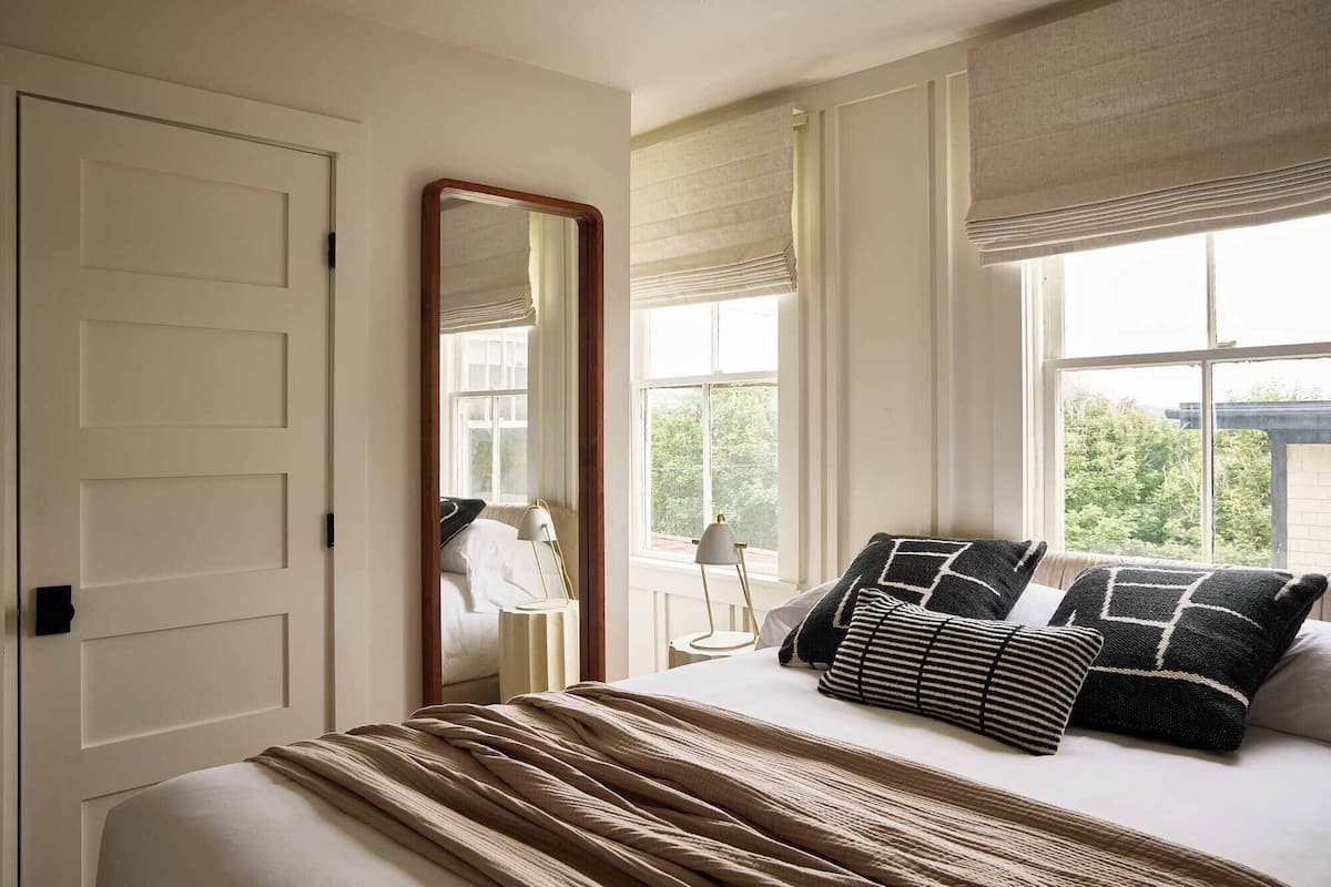 Un dormitorio con cama, un espejo grande y dos ventanas con persianas.