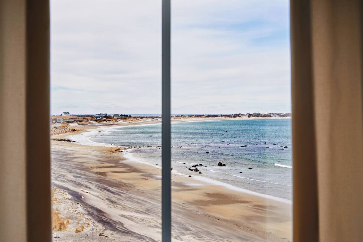 Vista de la playa a través de una ventana, con cielo despejado.