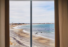 Vista de la playa a través de una ventana, con cielo despejado.