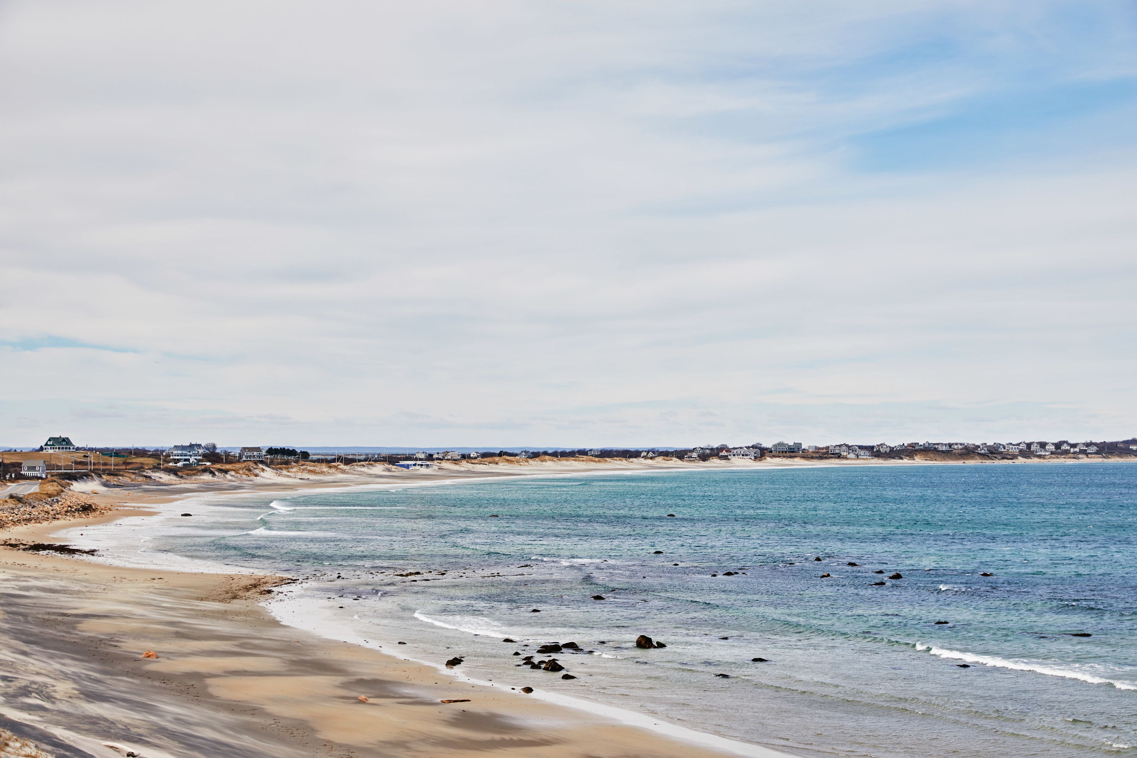 A coastal beach with a sandy shore, a calm sea, and a distant shoreline with buildings.