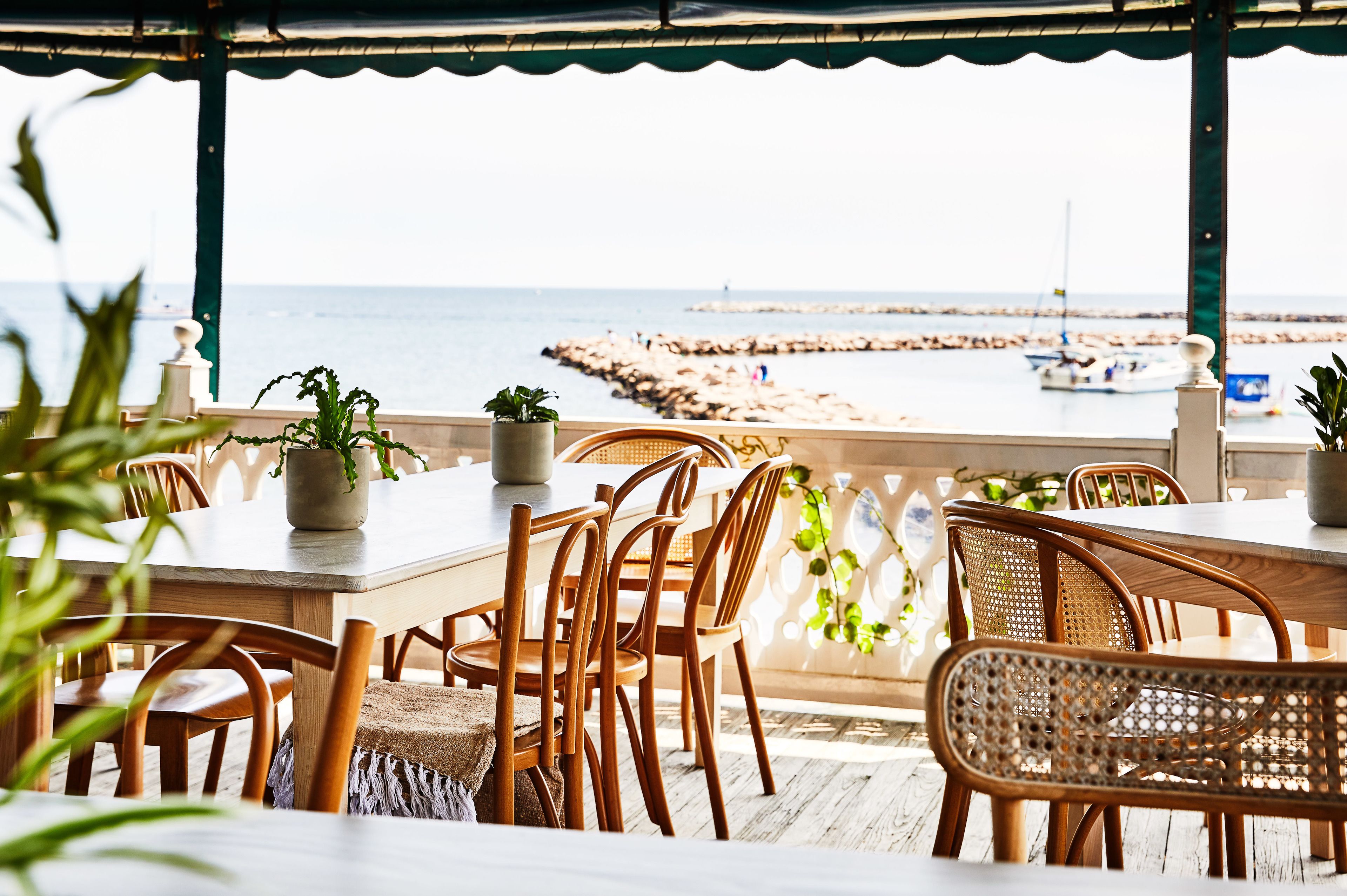 Un área de comedor al aire libre de madera con vista al mar y un muelle.