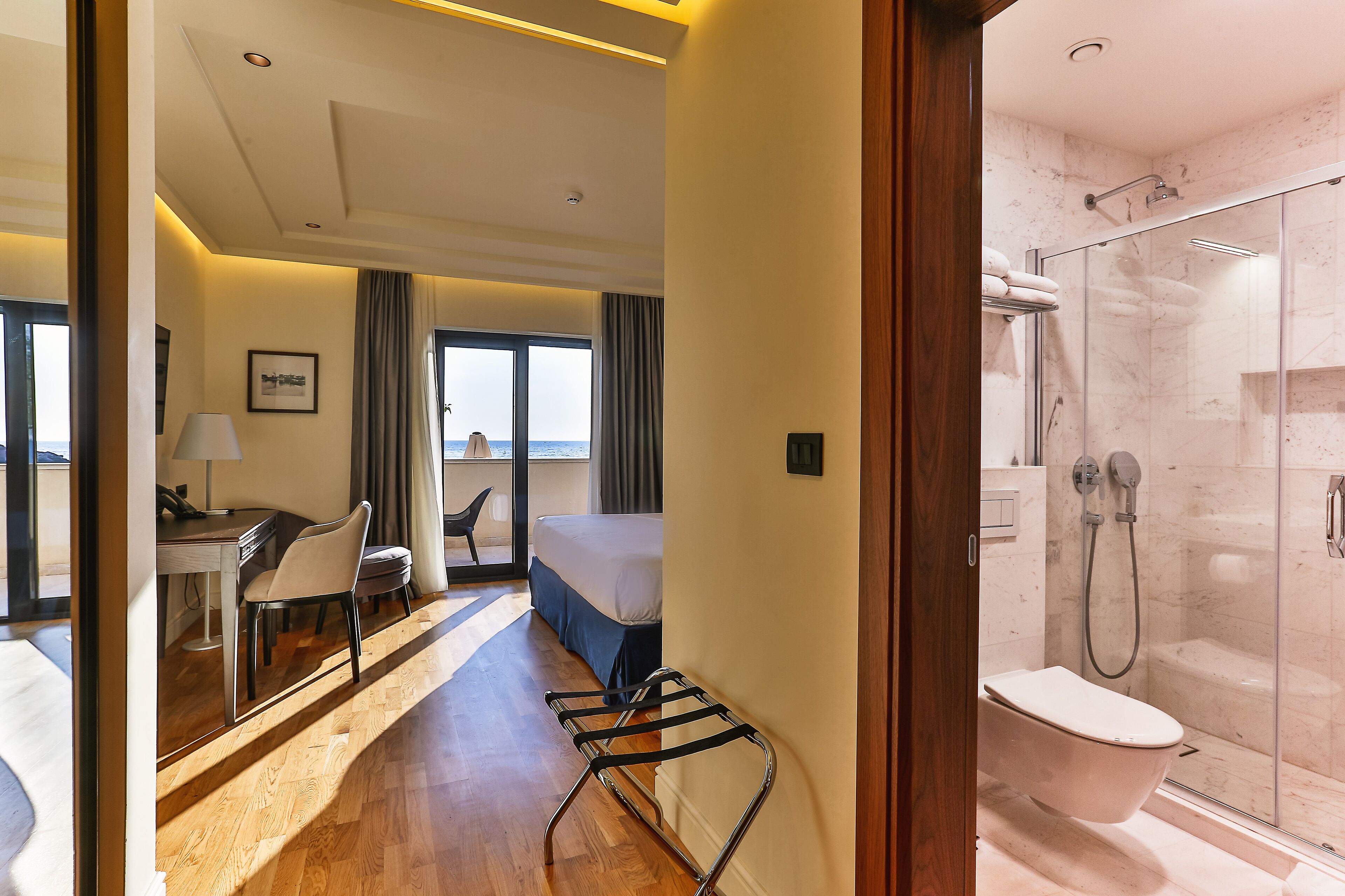 Habitación de hotel con cama, escritorio, silla, ducha y vista al mar.