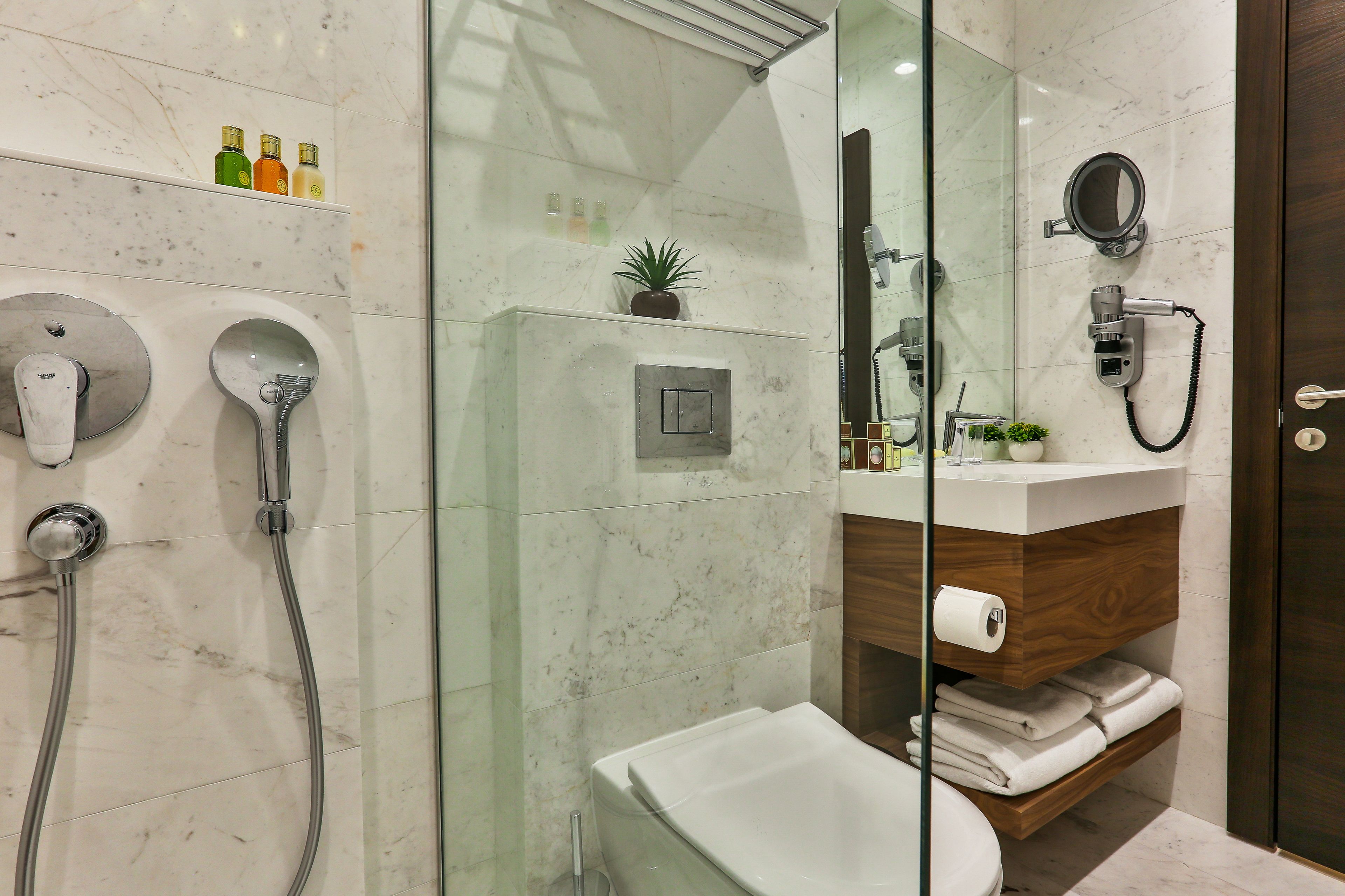 Un baño moderno con cabina de ducha de vidrio, inodoro blanco, tocador de madera y salpicadero de mármol.