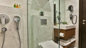 Un baño moderno con cabina de ducha de vidrio, inodoro blanco, tocador de madera y salpicadero de mármol.