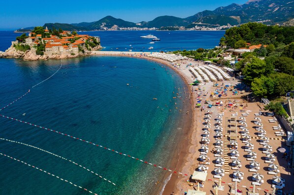 Un hôtel situé sur la côte, avec une plage, des bateaux et une chaîne de montagnes en arrière-plan.