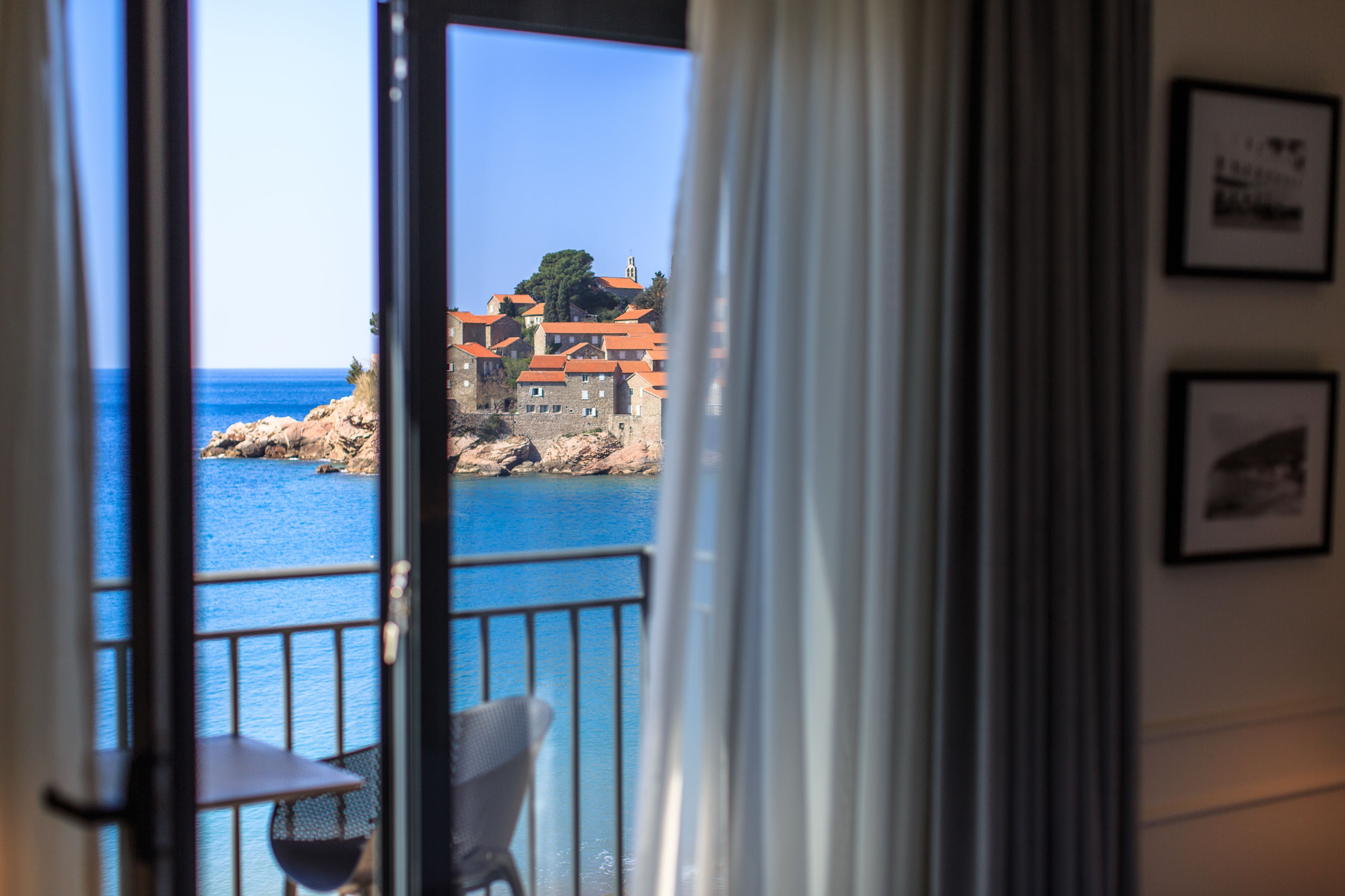 A view from a balcony overlooking a coastal town with buildings and a clear blue sea.