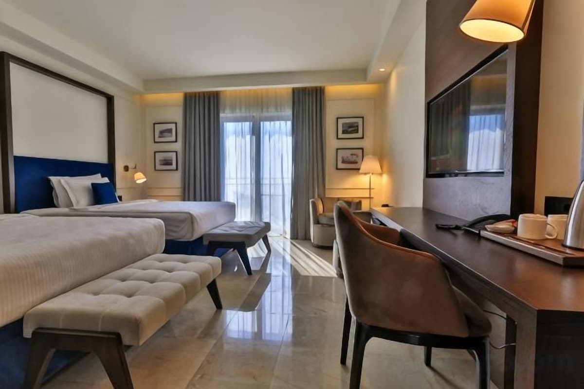 Une chambre d’hôtel avec deux lits, un bureau, une chaise, une lampe et un grand miroir.