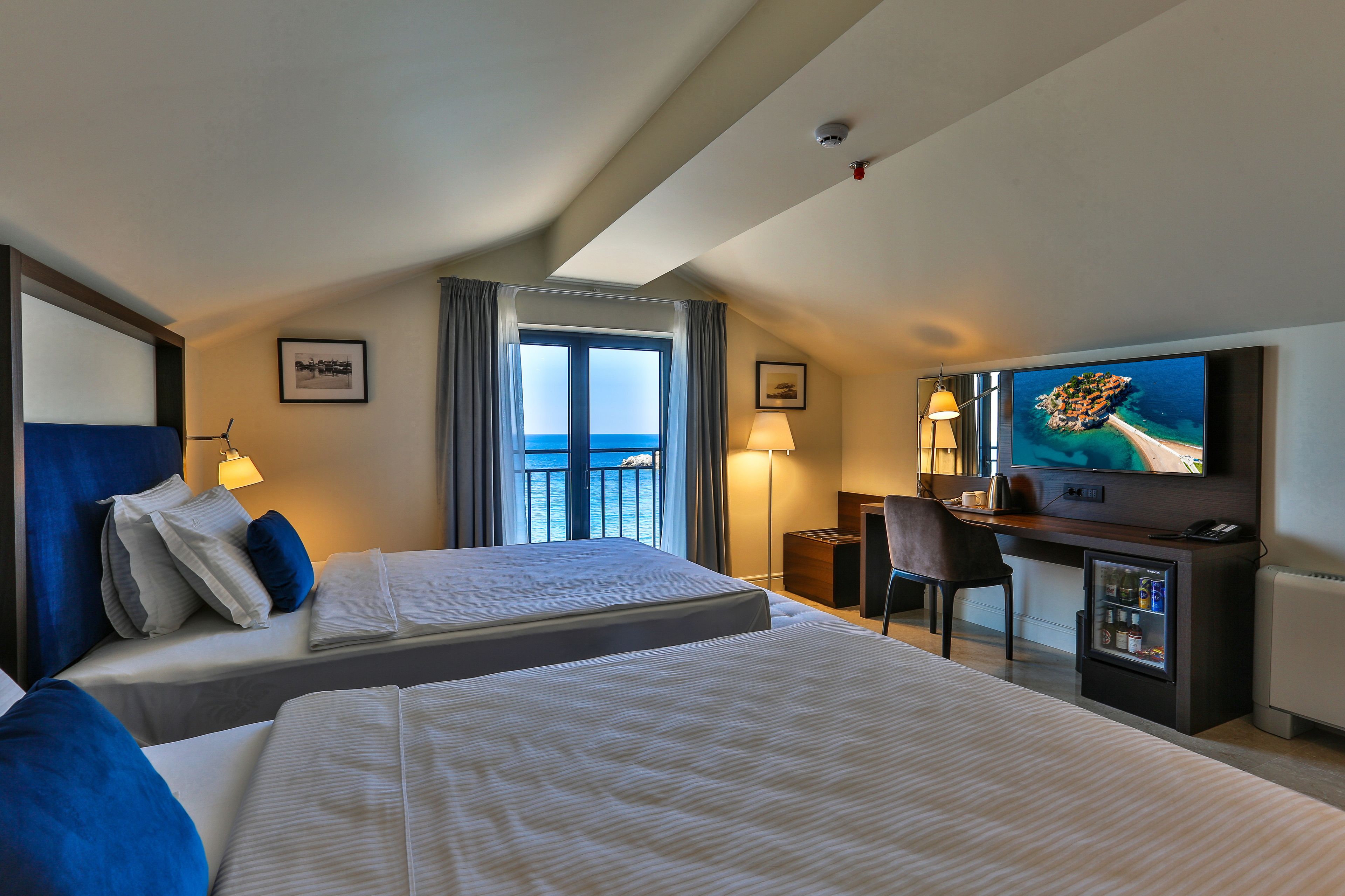 Une chambre d’hôtel avec deux lits, un bureau avec une télévision, un mini-réfrigérateur et une vue sur la mer.