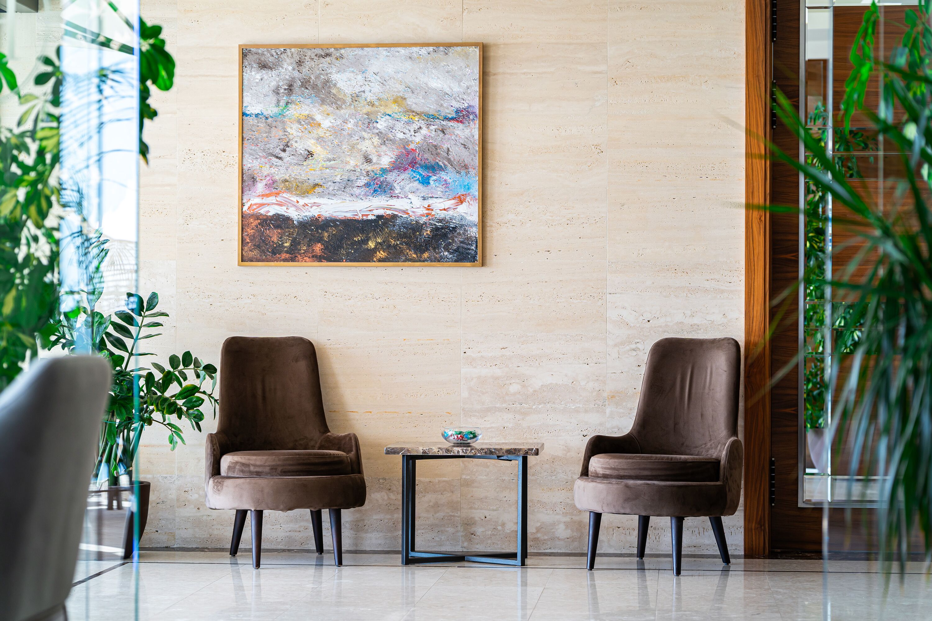 Un hall d’entrée avec deux fauteuils marron, une petite table sur laquelle se trouve un bol, et un grand tableau abstrait accroché au mur.