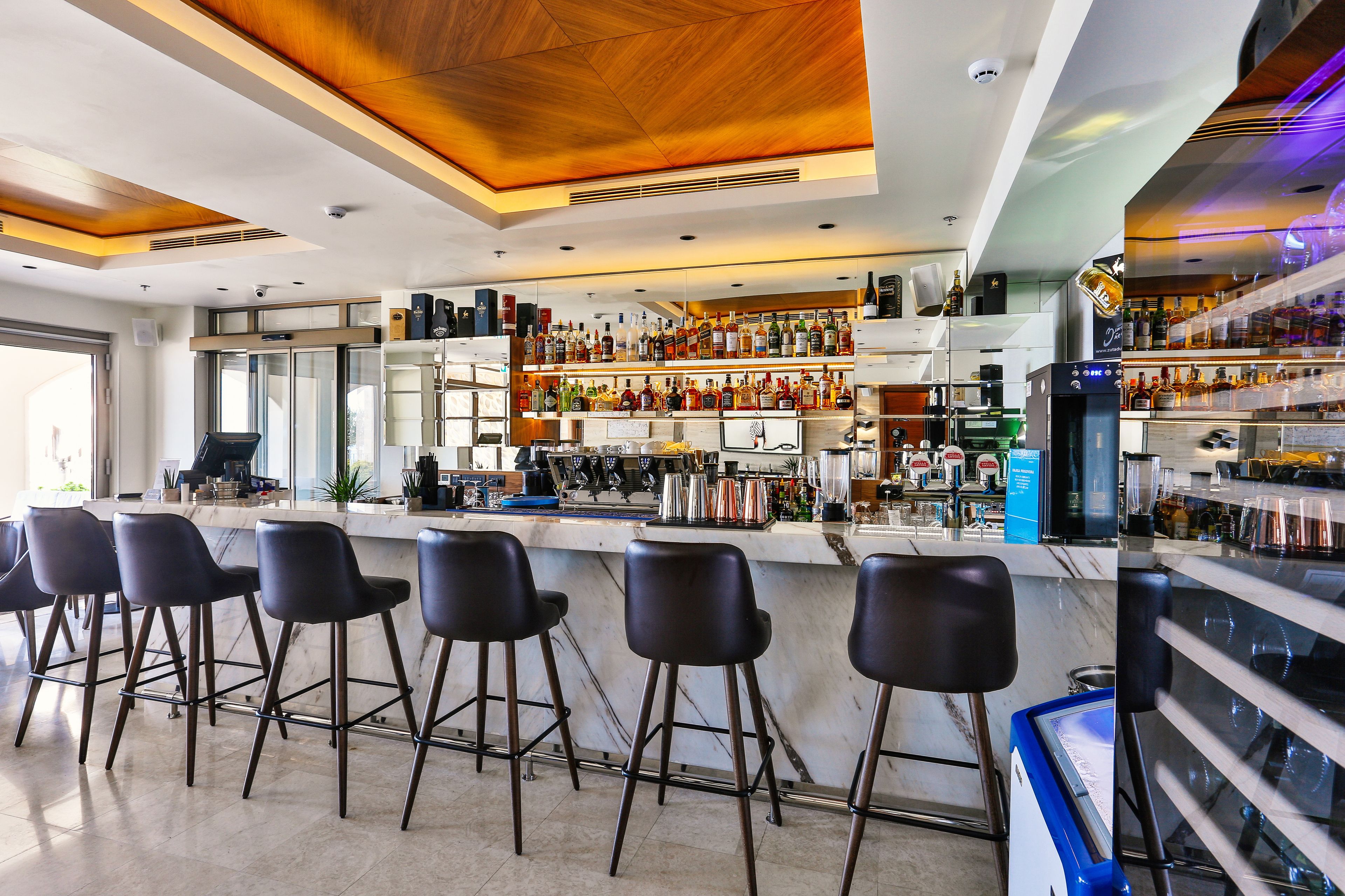Zona bar moderna con un bancone in marmo, sgabelli da bar neri e una selezione di bottiglie di liquore.