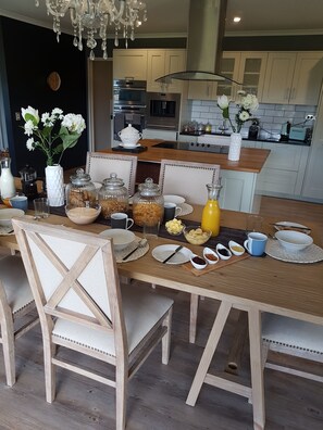 Una cocina moderna con una mesa de comedor de madera dispuesta para el desayuno, que incluye una cafetera, frascos de comida y un florero.