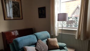 A teal sofa with three cushions, a wooden headboard, a small table, and a floor lamp. - Lingdale 4 Bedroom House & Trundlebed Option (Saltburn-by-the-Sea)