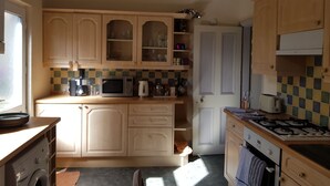 A compact kitchen with wooden cabinets, a microwave, a kettle, and a gas stove. - Lingdale 4 Bedroom House & Trundlebed Option (Saltburn-by-the-Sea)