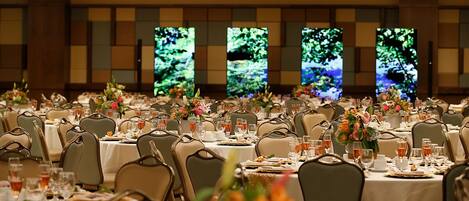 Un salón de banquetes con varias mesas redondas, cada una dispuesta con sillas, vasos y centros de mesa florales.