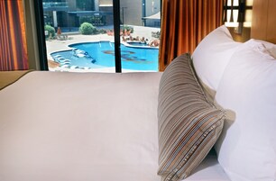 Una habitación de hotel con una cama grande, un almohadón a rayas y vistas a una piscina exterior.