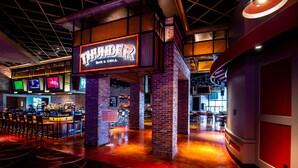 Zona de bar con un letrero de neón que dice "THUNDER BAR & GRILL" y una barra con taburetes.