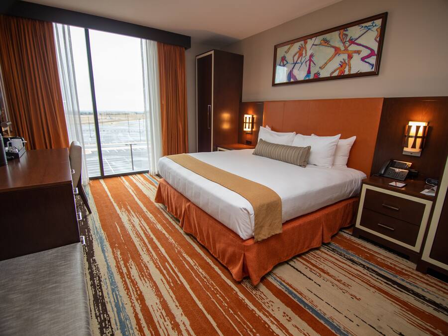 A hotel room with a large bed, a desk, a chair, a nightstand with a phone, and a painting on the wall.