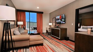 Habitación de hotel con sofá, televisión, escritorio y vistas a la ciudad.