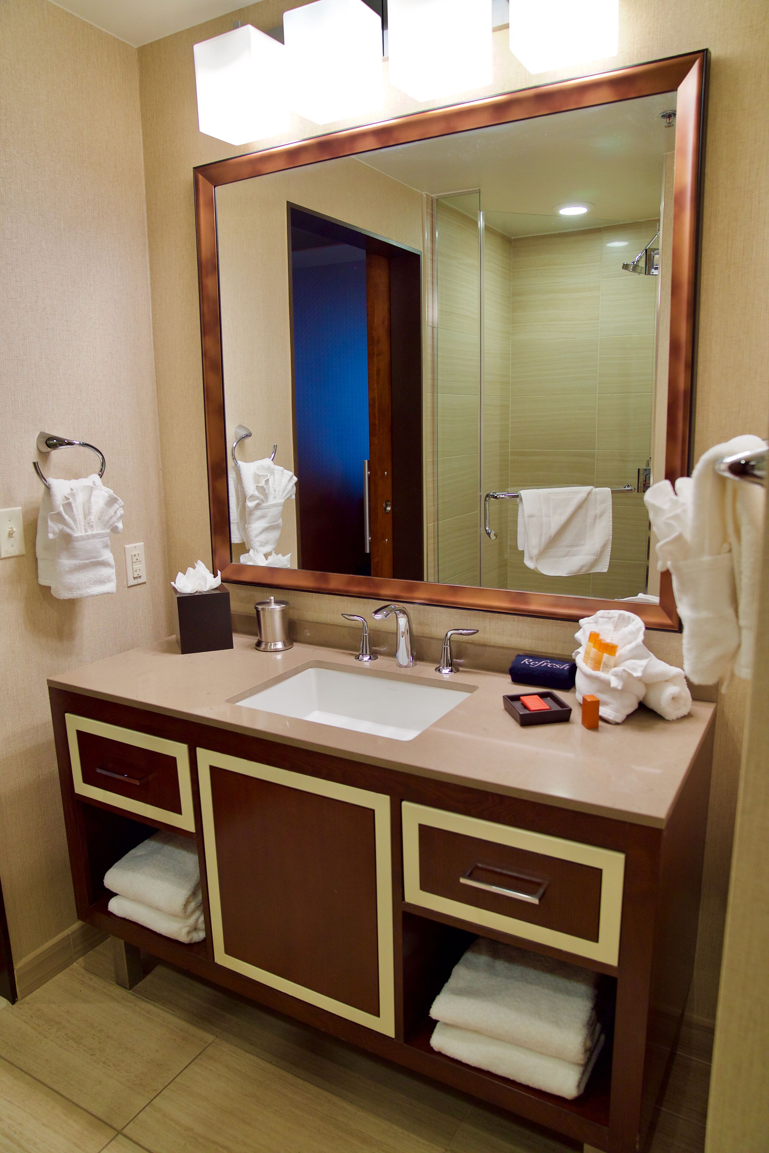 A hotel bathroom with a large mirror, a sink, and a vanity with storage drawers.