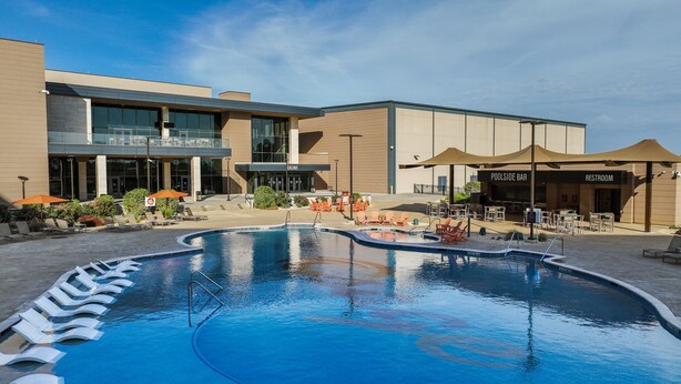 Zona de piscina con sillones de descanso y un edificio que alberga un casino y un bar junto a la piscina.